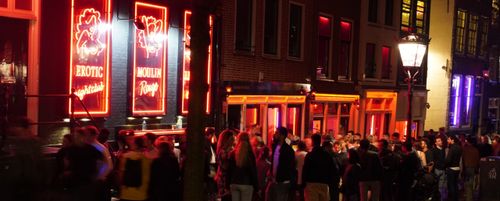 Menschen stehen in der Nacht vor dem Moulin Rouge an, einem mit Neonfarben beleuchteten Nachtclub
